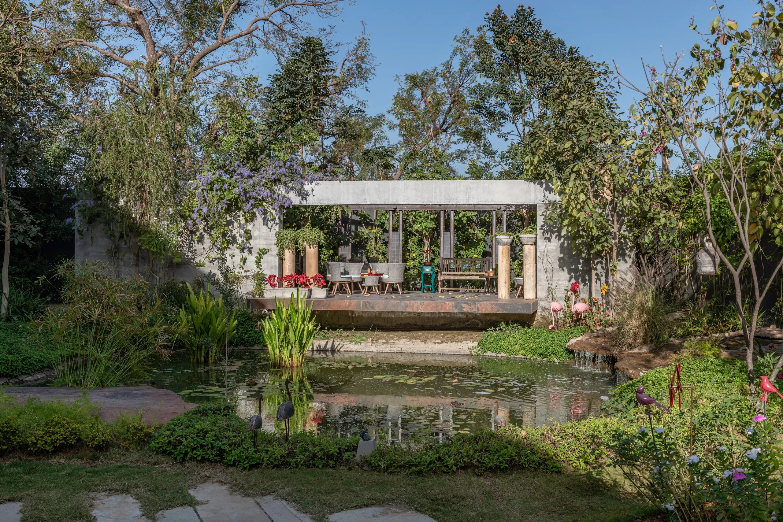 Dusk view of the raised dining pergola beside the courtyard water body, garden lit by low lamps
