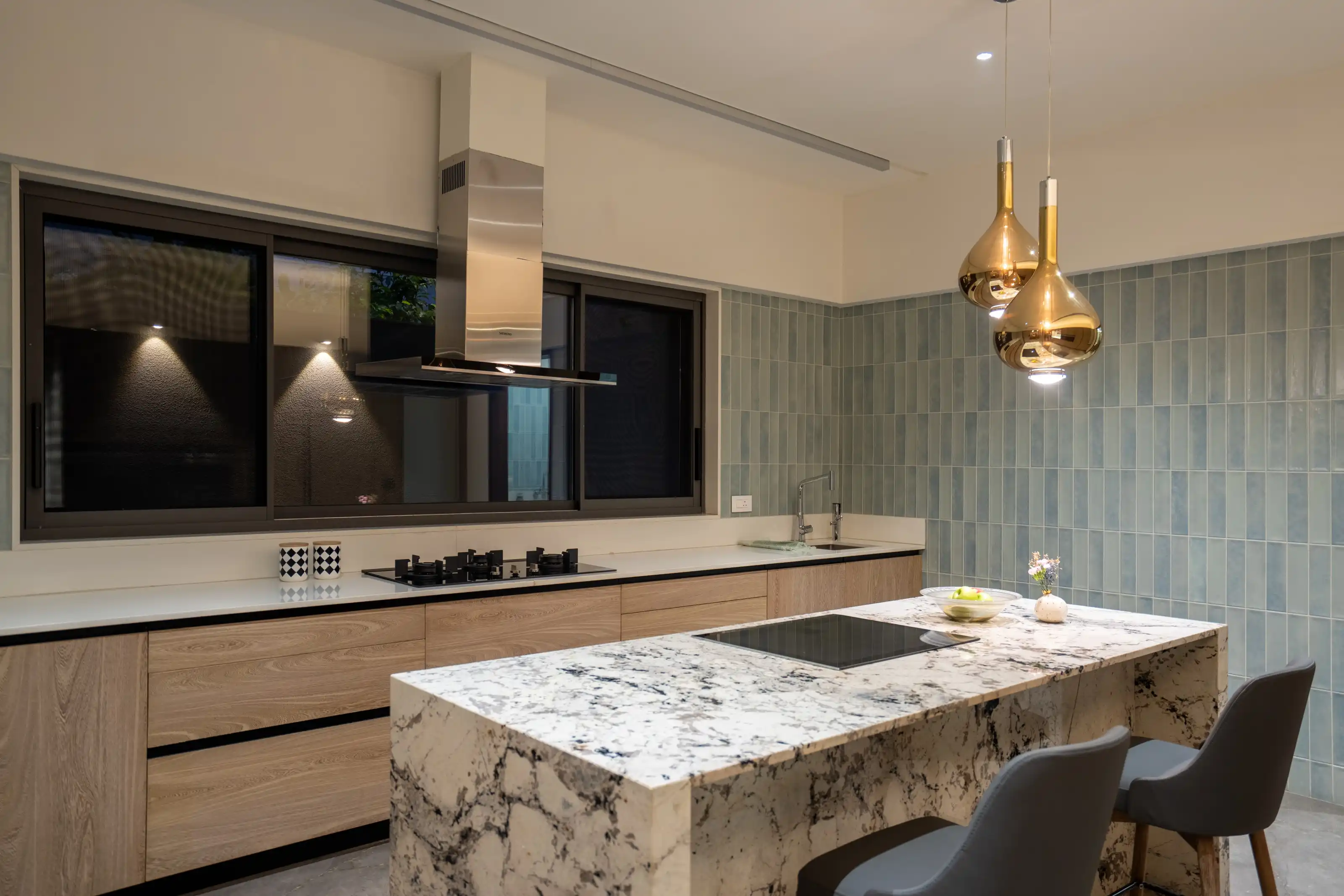 Kitchen island in patterned marble beneath twin gold teardrop pendant lights and sage tile