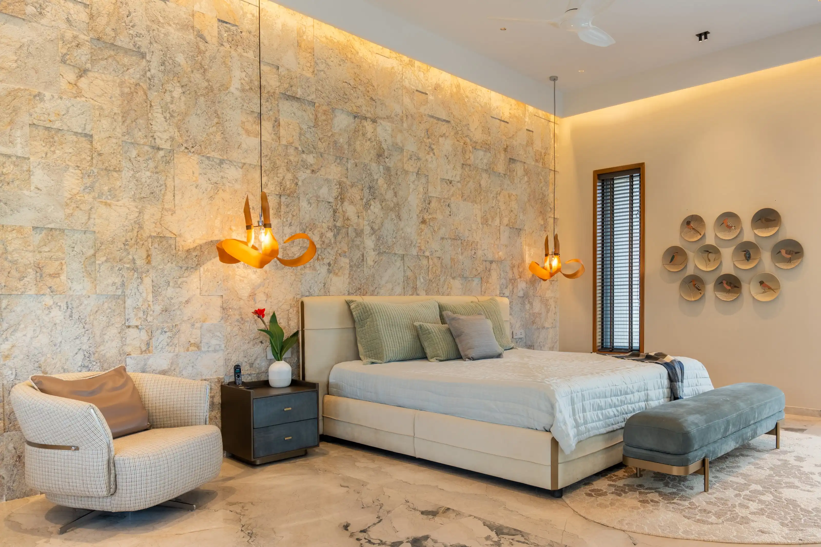 Stone-clad bedroom with brass-ribboned pendant lights and a wall of framed bird plates