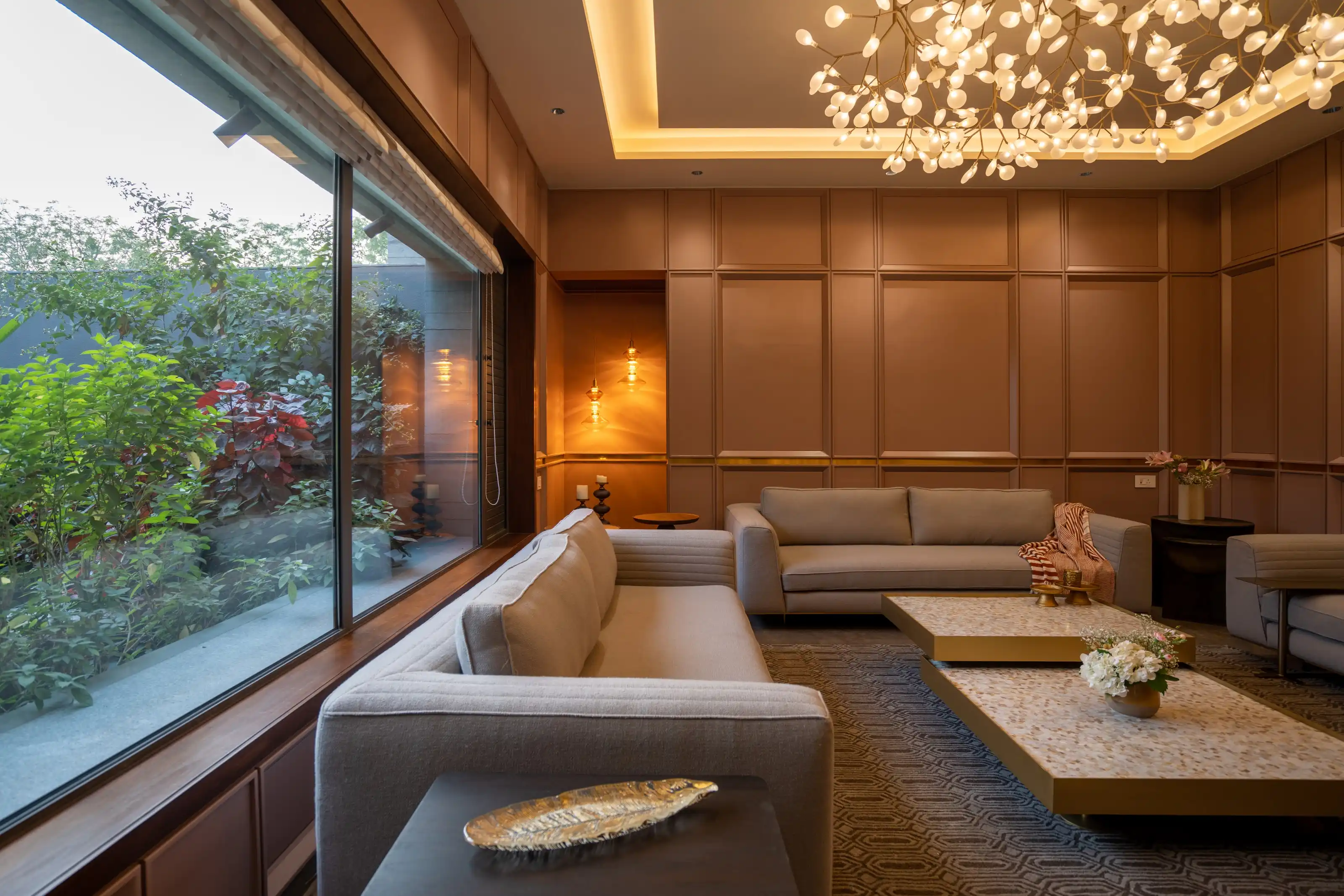 Panelled beige living room with cream sofas beneath a cluster chandelier of glass leaves