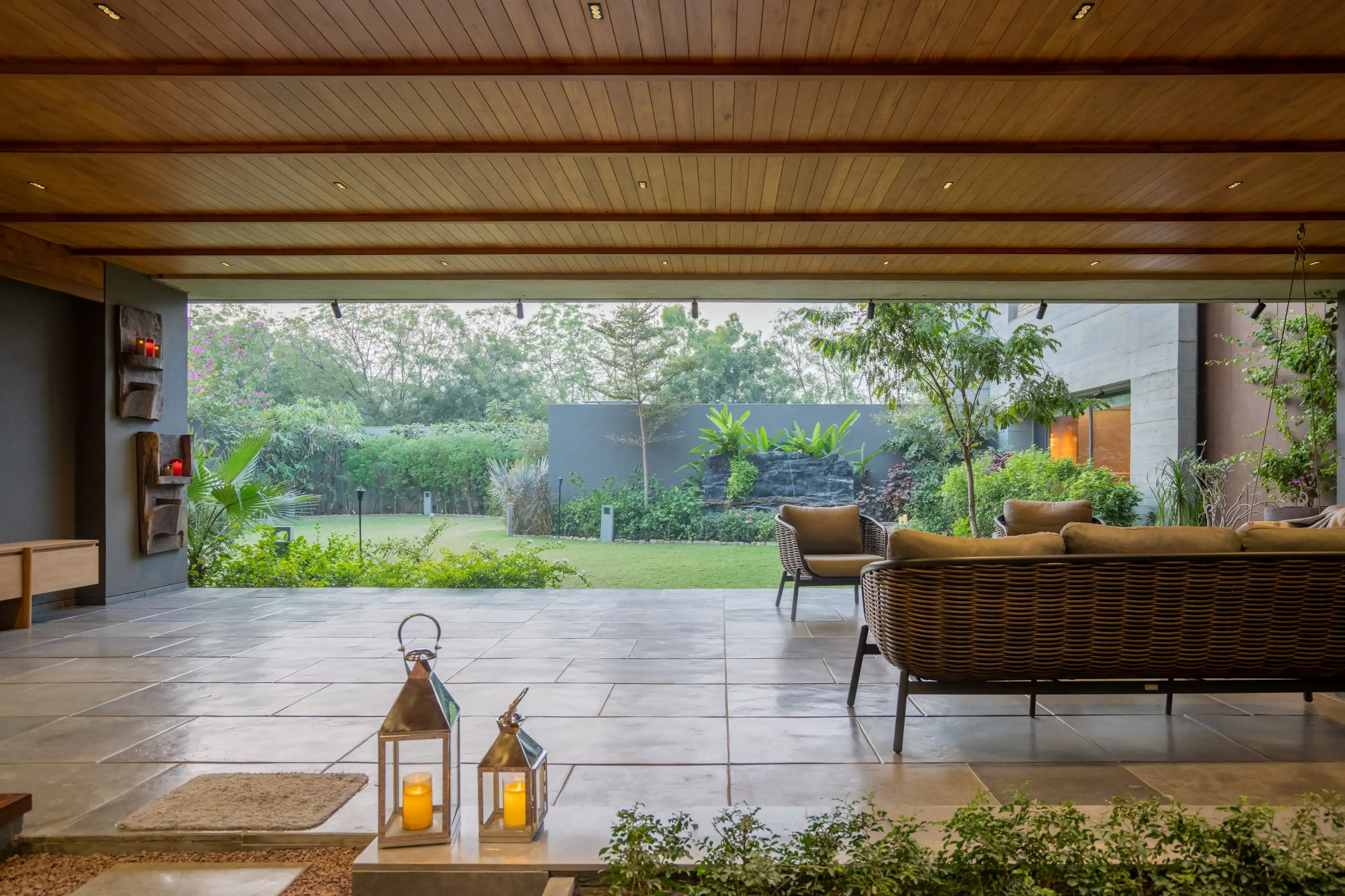 Covered courtyard patio with woven rattan sofas, brass lanterns and a garden wall feature