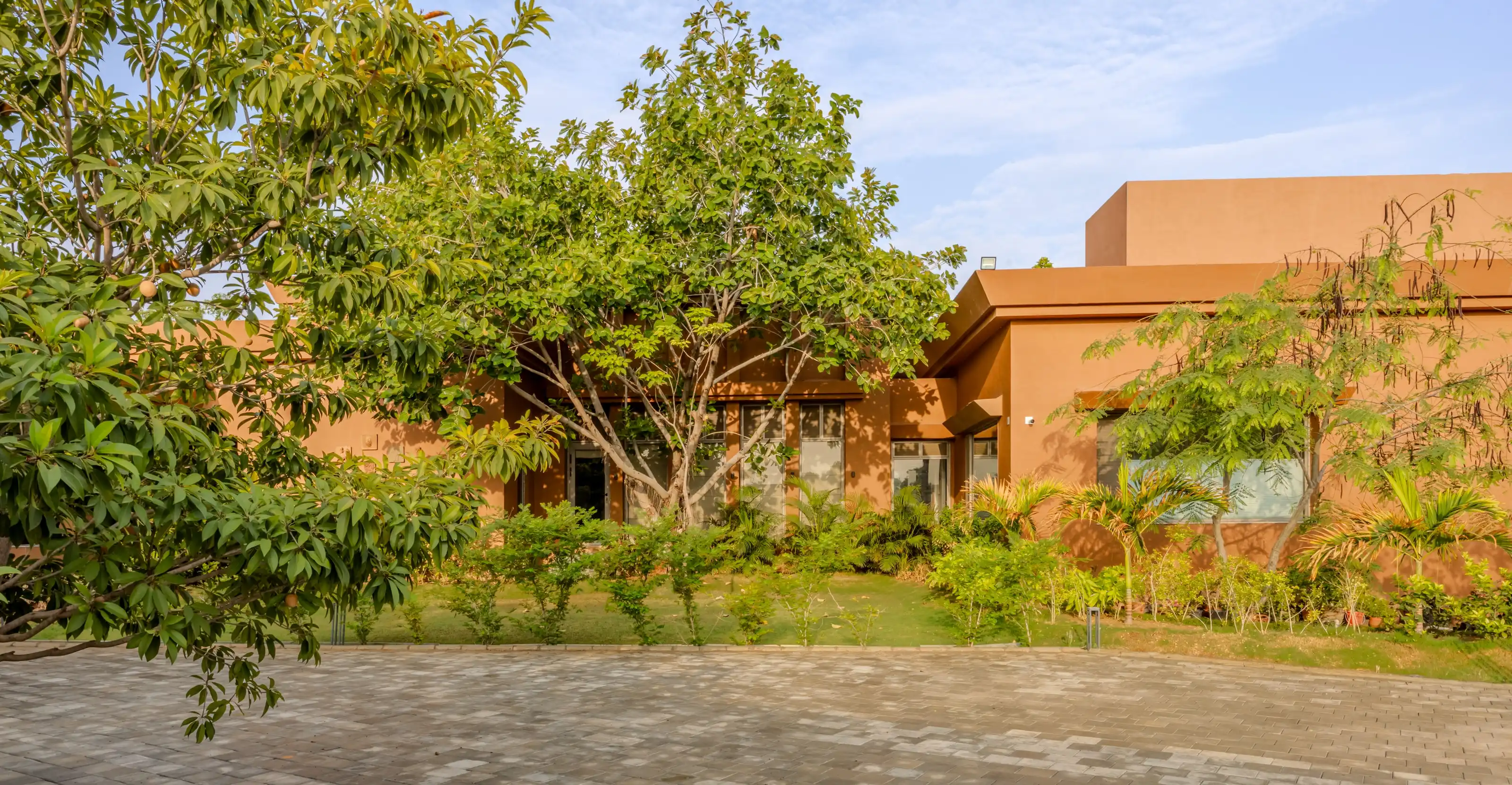 Wide exterior view of the ochre farmhouse nestled among mature trees, seen from the garden