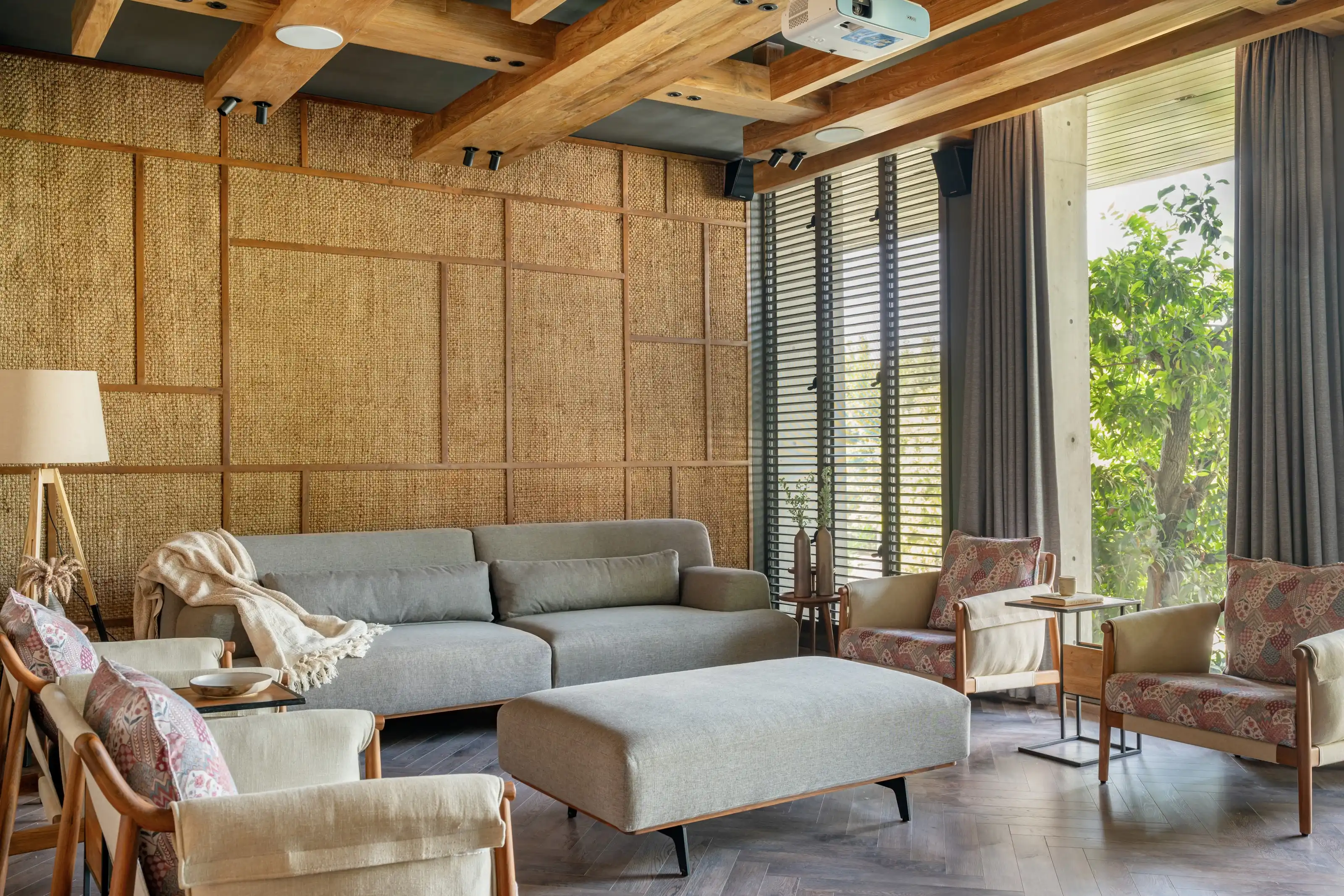 Living room walled in woven rattan panels with grey sofas facing a garden of curtained glass doors