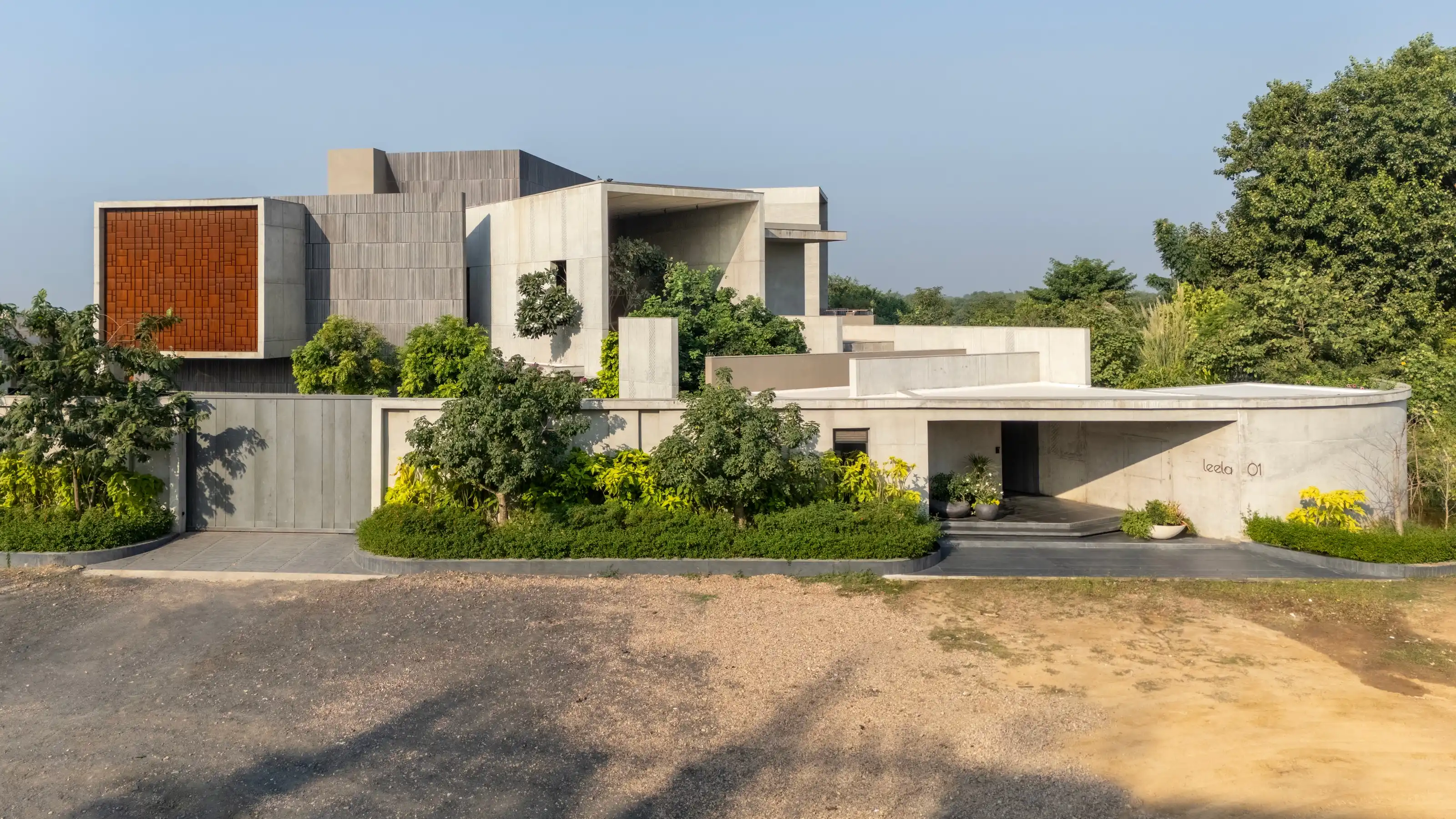 Curved concrete boundary wall and red laterite entrance screen leading to the carport