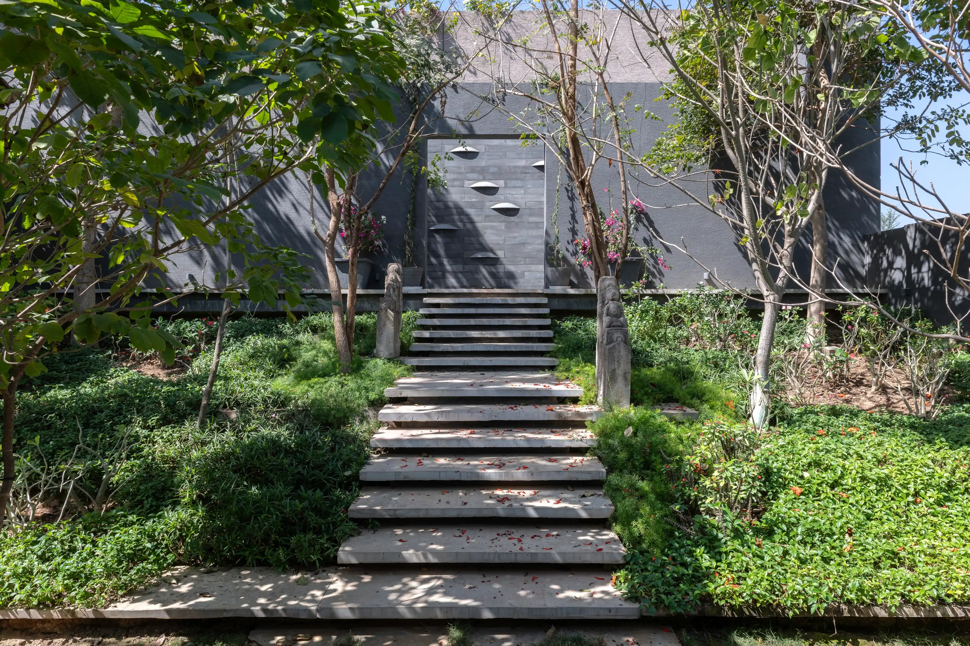 Dark stone facade approached across a broad ceremonial stair set into deep planting
