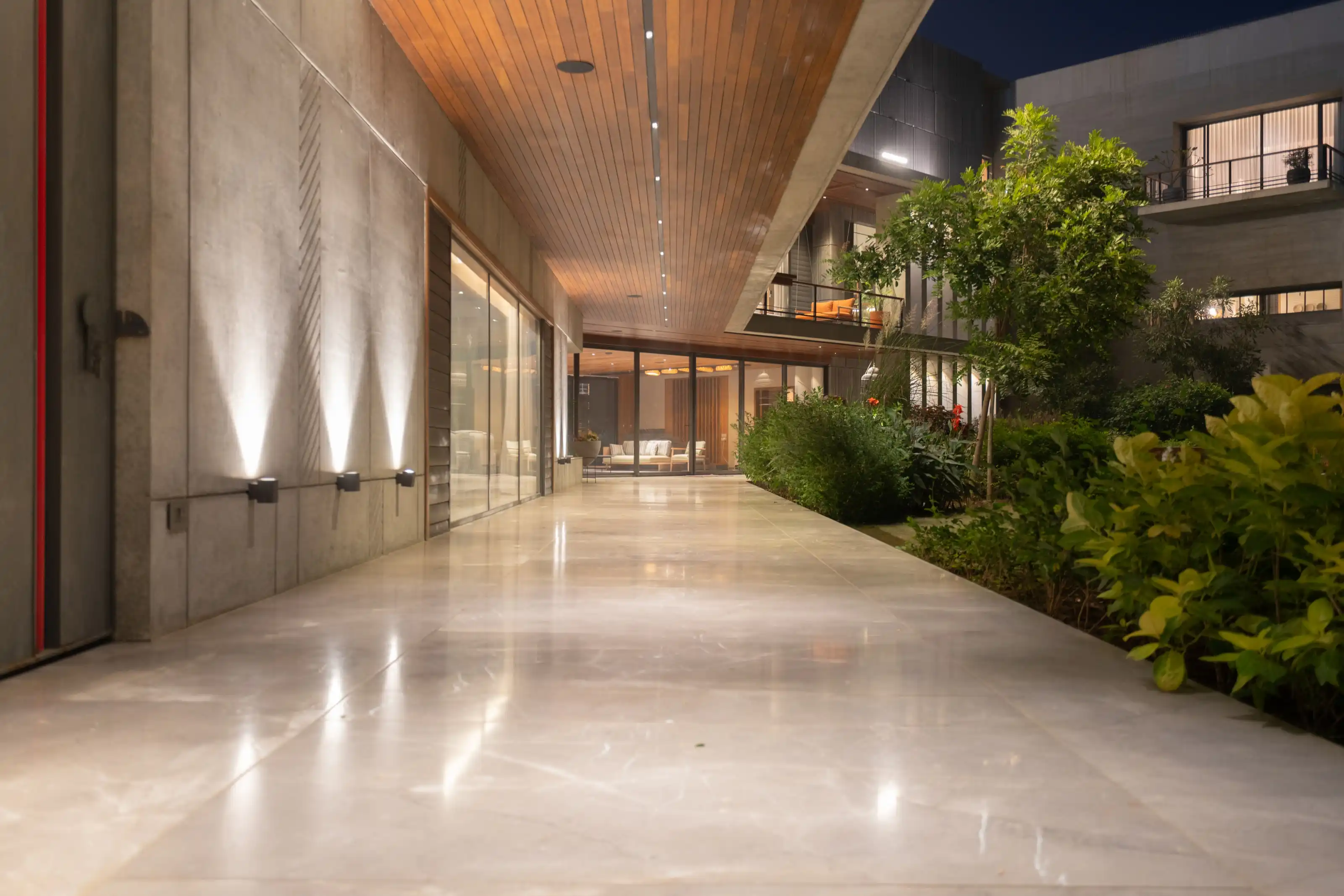 Night view along a wood-soffited concrete corridor beside a lit garden