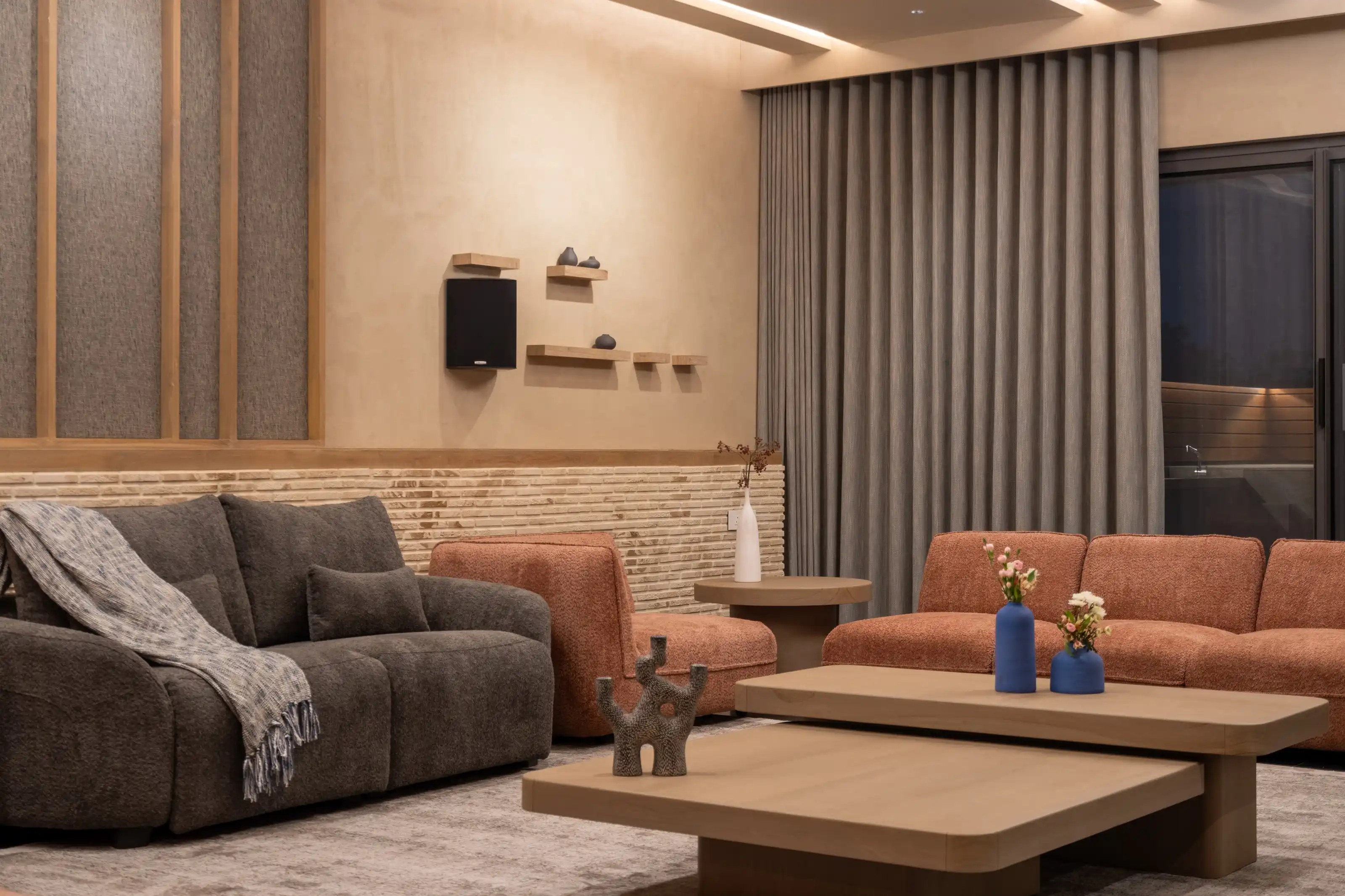 Living room with a charcoal sofa and terracotta armchairs against a ribbed timber and brick wall