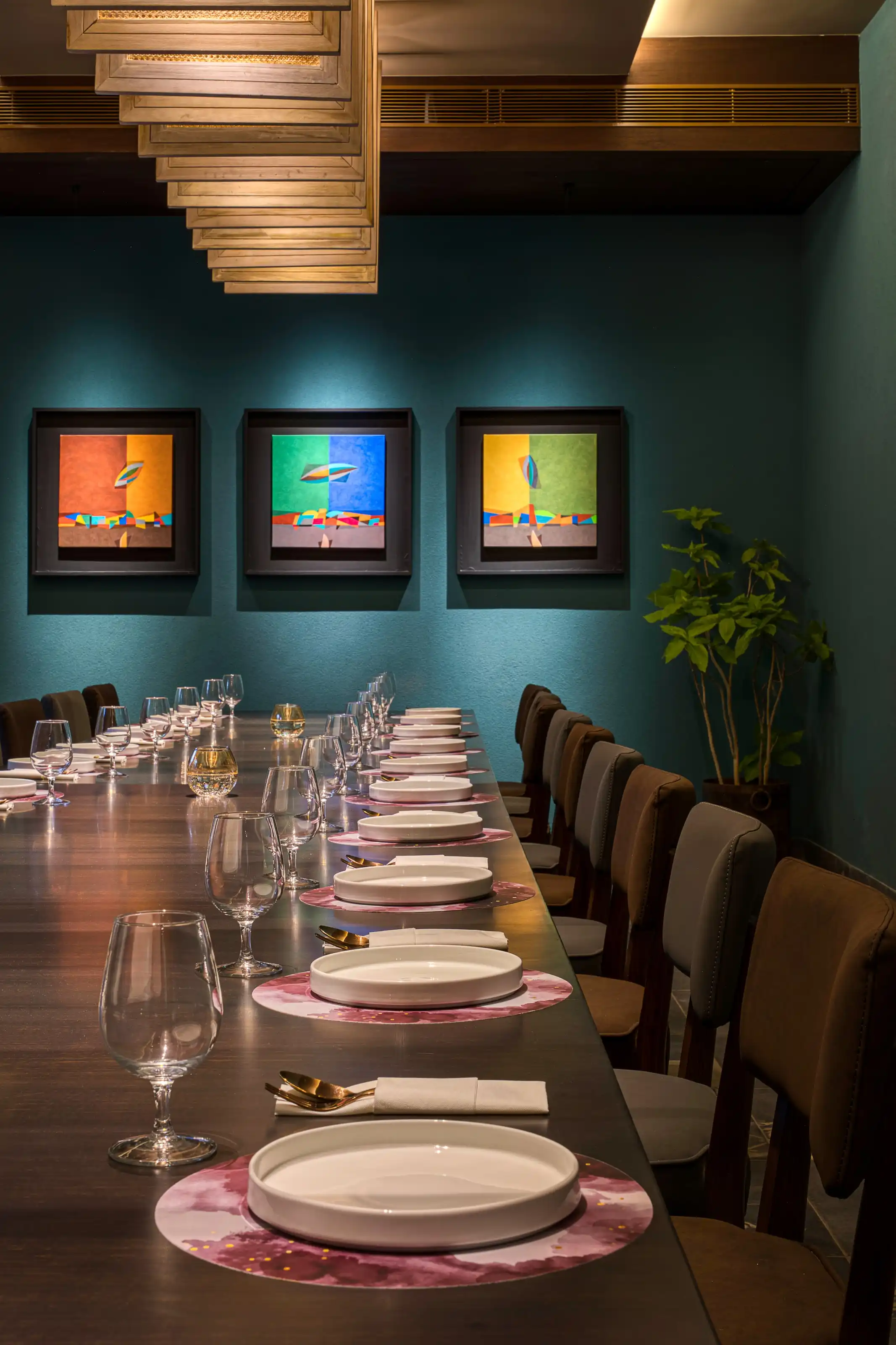 Long private dining table set for many guests beneath a teal wall hung with abstract art