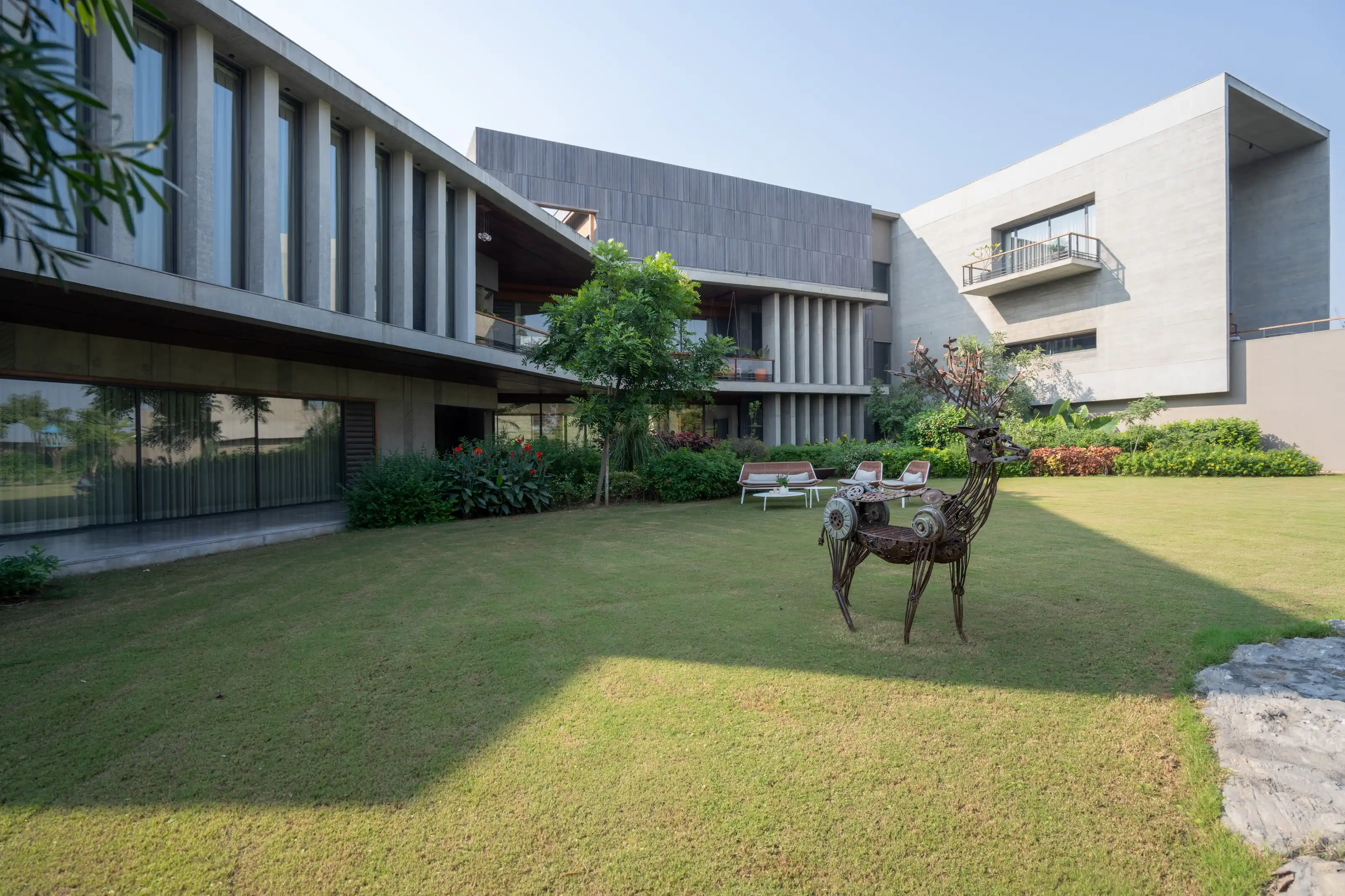 Board-formed concrete wings of the house stepping around a lawn with a sculpted metal deer